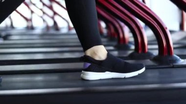 Spor salonunda koşu bandı. Spor ayakkabılarıyla spor salonundaki koşu bandında yürüyen bacaklar. Kardiyo çalışması. Spor yapan bir kız. Koşu bandında yavaş adımlarla yürüyen bacaklar, yakın plan. Spor.