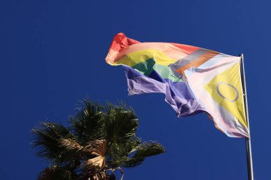 İlerleme Gururu Bayrağı 'nın cinsiyetler arası tasarımı. Gökkuşağı LGBT bayrağı mavi gökyüzüne karşı. Rüzgarda dalgalanan bayrak. Lezbiyen, gey, biseksüel, transseksüel anlamına gelen bir kısaltma.