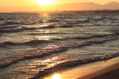 Denizde gün batımı. Balear Denizi, Salou, İspanya. Kumsal, deniz, küçük dalgalar. Sahilde akşam manzarası. Denizde tatil.