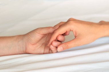 Eşcinsel ilişkiler, lezbiyenler. Beyaz çarşaflar üzerinde birbirine dokunan iki kadın eli. Yatakta iki kadın eli var. Yakın plan. LGBTQ, aşk konsepti.