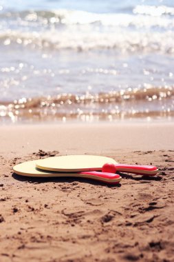 Kumsalda tenis raketleri ve kumların üzerinde duran bir top. Plaj tenisi. Suya yakın açık havada aktif yaz tatili. Kumsalda spor eğlencesi kavramı. Spor ve oyun