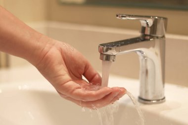 Banyo musluğu, ellerini yıkayan kadın, yakın plan. Banyoda ellerini lavaboda yıkayan bir kadın. Kişisel hijyen. Suyun altında ellerini yıkamak. Sağlık hizmeti konsepti. Ellerini temiz tut.