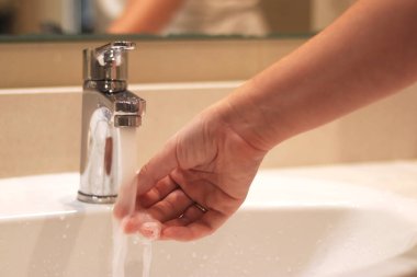 Banyo musluğu, ellerini yıkayan kadın, yakın plan. Banyoda ellerini lavaboda yıkayan bir kadın. Kişisel hijyen. Suyun altında ellerini yıkamak. Sağlık hizmeti konsepti. Ellerini temiz tut.