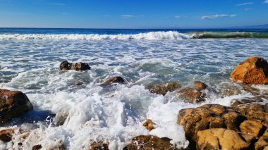 Balear Denizi, Salou, İspanya. Plaj, turkuaz şeffaf deniz, küçük dalgalar. Sahildeki manzara, kayalar. Denizde tatil.