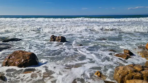 Balear Denizi, Salou, İspanya. Plaj, turkuaz şeffaf deniz, küçük dalgalar. Sahildeki manzara, kayalar. Denizde tatil.