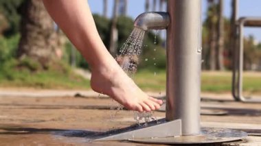 Plaj duşu. Kız sahildeki musluk suyuyla ayaklarını kumdan yıkıyor. İnsanlar sahilden ayrılırken ayaklarını yıkarlar. Kadın ayaklarını yakın çekimde yıkıyor. Deniz kenarında kumsal yağmuru