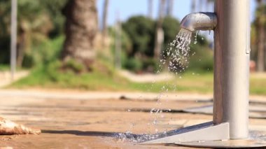 Plaj duşu. Kız sahildeki musluk suyuyla ayaklarını kumdan yıkıyor. İnsanlar sahilden ayrılırken ayaklarını yıkarlar. Kadın ayaklarını yakın çekimde yıkıyor. Deniz kenarında kumsal yağmuru