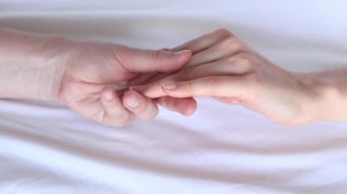 Eşcinsel ilişkiler, lezbiyenler. Beyaz çarşaflar üzerinde birbirine dokunan iki kadın eli. Yatakta iki kadın eli var. Yakın plan. LGBTQ, aşk konsepti