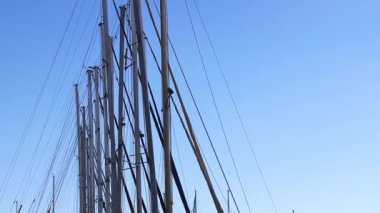 Mavi gökyüzüne karşı küçük yatların direkleri. Birçok yat, parlak gökyüzüne hafifçe sallanır. Spor ve eğlence.