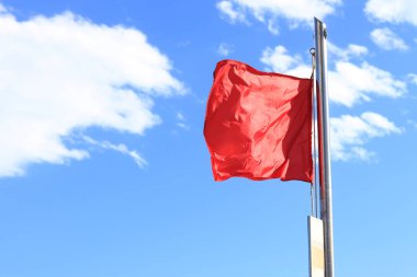 Gökyüzüne karşı kırmızı bayrak. - Yüzmek yasaktır. Bayrak yakın plan. Rüzgarda dalgalanan kırmızı bayrak denizde büyük dalgalar olduğunu gösteriyor. Kırmızı uyarı bayrağı turistlerin yüzmesini yasaklıyor