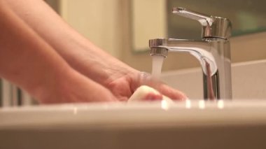 Banyo musluğu, ellerini yıkayan kadın, yakın plan. Banyoda ellerini lavaboda yıkayan bir kadın. Kişisel hijyen. Suyun altında ellerini yıkamak. Sağlık hizmeti konsepti. Ellerini temiz tut.