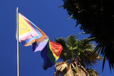 İlerleme Gururu Bayrağı 'nın cinsiyetler arası tasarımı. Gökkuşağı LGBT bayrağı mavi gökyüzüne karşı. Rüzgarda dalgalanan bayrak. Lezbiyen, gey, biseksüel, transseksüel anlamına gelen bir kısaltma.