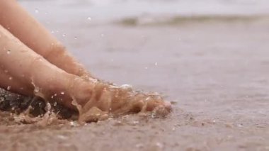 Sahilde kadın bacakları, deniz, yakın plan. Deniz dalgalarının arka planında çıplak ayaklar. Kadın bacakları yakın çekim, plaj tatili. Kumsalda dinlenmek, yaz tatili.