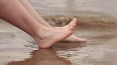 Sahilde kadın bacakları, deniz, yakın plan. Deniz dalgalarının arka planında çıplak ayaklar. Kadın bacakları yakın çekim, plaj tatili. Kumsalda dinlenmek, yaz tatili.