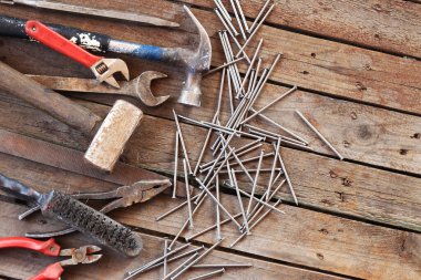 Ahşap bir yüzeyde eski bir el aleti. Ayarlanabilir anahtar, anahtar, balta, çekiç, çivi ve pense. Tamir ve inşaat için aletler, üst manzara. İnşaat geçmişi. Eski paslı bir aletin bileşimi