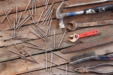 Ahşap bir yüzeyde eski bir el aleti. Ayarlanabilir anahtar, anahtar, balta, çekiç, çivi ve pense. Tamir ve inşaat için aletler, üst manzara. İnşaat geçmişi. Eski paslı bir aletin bileşimi