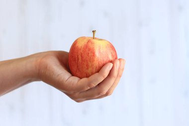 Hafif ahşap arka planda, kadının elinde olgun bir elma. Elma ile yakın çekim. Sağlıklı beslenme, vitamin ve diyet kavramı. Meyveler. Beyaz kadın eli elmayı gösteriyor