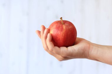 Hafif ahşap arka planda, kadının elinde olgun bir elma. Elma ile yakın çekim. Sağlıklı beslenme, vitamin ve diyet kavramı. Meyveler. Beyaz kadın eli elmayı gösteriyor