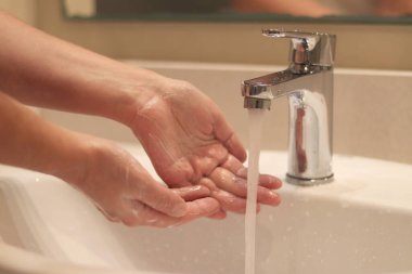 Kadın ellerini yıkıyor, yakın plan. Banyo musluğu. Banyoda ellerini lavaboda yıkayan bir kadın. Kişisel hijyen. Suyun altında ellerini yıkamak. Sağlık hizmeti konsepti. Ellerini temiz tut.
