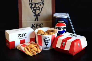 Kyiv, Ukrayna - 20 Ekim 2024: KFC. Striptiz kovası, burger, standart patates kızartması, Peps ve bir kese kağıdı. KFC fast food restoranı. Karanlık bir arka planda fast food. KFC 'de özelleştirilmiş menü ögeleri