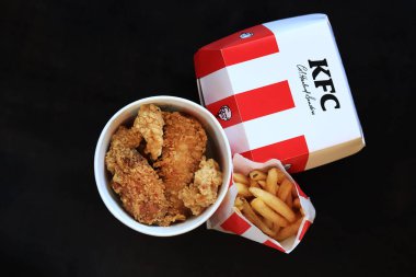 Kyiv, Ukrayna - 20 Ekim 2024: KFC. Şeritli kova, karton kutuda burger ve patates kızartması. KFC fast food restoranı. Karanlık arka planda fast food. KFC yiyeceklerinin üst görünümü