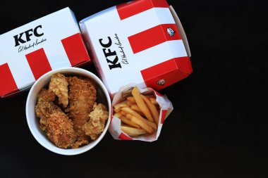 Kyiv, Ukrayna - 20 Ekim 2024: KFC. Şeritli kova, karton kutuda burger ve patates kızartması. KFC fast food restoranı. Karanlık arka planda fast food. KFC yiyeceklerinin üst görünümü