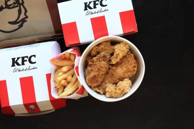 Kyiv, Ukrayna - 20 Ekim 2024: KFC. Şeritli kova, karton kutuda burger ve patates kızartması. KFC fast food restoranı. Karanlık arka planda fast food. KFC yiyeceklerinin üst görünümü