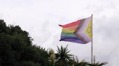 Salou, İspanya - 18 Eylül 2024: İlerleme Gururu Bayrağının Cinsiyetler Arası Kapsamlı Yeniden Tasarımı. Gökkuşağı LGBT bayrağı gökyüzüne karşı. Kötü havada rüzgarda dalgalanan bayrak
