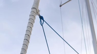 Gökyüzüne doğru kayan yelken. Yelkenli bir yatta seyir halindeler. Küçük bir yatın yelkenlisine yakın çekim. Direkli tekneler. Yelkenli teknesinde beyaz yelkenli
