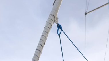 Gökyüzüne doğru kayan yelken. Yelkenli bir yatta seyir halindeler. Küçük bir yatın yelkenlisine yakın çekim. Direkli tekneler. Yelkenli teknesinde beyaz yelkenli