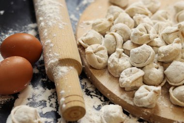 Çiğ hamur tatlısı, seçici odaklanma. Pelmeni, un, yumurta ve tahta raptiye. Tahta üzerinde et pelmeni ya da ravioli, karanlık masa. Geleneksel Slav yemeği. Gıda arkaplanı