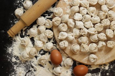 Çiğ pelmeni, üst görüş, düz yatış. Pelmeni, un, yumurta ve tahta raptiye. Tahta tahtada etli börek ya da ravioli, karanlık masa. Geleneksel Slav yemeği. Gıda arkaplanı