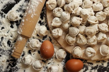 Çiğ pelmeni, üst görüş, düz yatış. Pelmeni, un, yumurta ve tahta raptiye. Tahta tahtada etli börek ya da ravioli, karanlık masa. Geleneksel Slav yemeği. Gıda arkaplanı