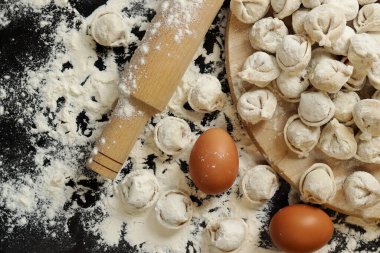 Çiğ pelmeni, üst görüş, düz yatış. Pelmeni, un, yumurta ve tahta raptiye. Tahta tahtada etli börek ya da ravioli, karanlık masa. Geleneksel Slav yemeği. Gıda arkaplanı