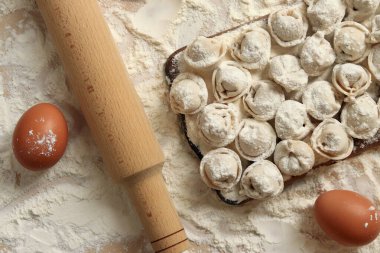 Pişmemiş hamur tatlısı, en iyi manzara, düz yatak. Hamur köftesi, un, yumurta ve tahta raptiye. Hamur köftesi ya da ahşap tahtada ravioli, un kaplı bir masa. Geleneksel Slav yemeği. Gıda arkaplanı