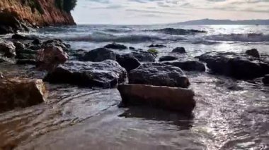 Yer seviyesinden deniz kıyısı, suyun yakınındaki kayalar, taşlar. Balear Denizi, Salou, İspanya. Kumsal, deniz, küçük dalgalar. Sahil. Denizde tatil.