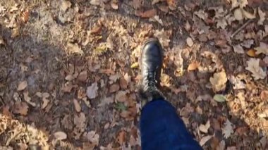 Kotlu kadın bacakları ve sonbahar botları sarı sonbahar yapraklarıyla kaplı bir orman yolunda yürüyor. Yere düşen yapraklarla kaplı birinci şahıs görüntüsü. Parkta yürü. Turizm