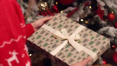 Elinde bir yayla yeni yıl hediyesinin yakın çekimi. Kutuda hediye paketi ve bir fiyonk. Noel ya da yeni yıl. Almak ya da hediye vermek için. - Sürpriz. Kız hediye paketinde bir kutuyu inceliyor.