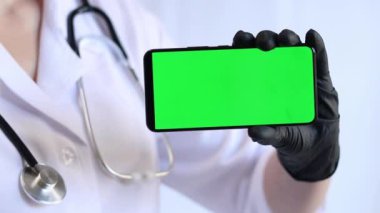 Yeşil ekranlı telefonu olan bir sağlık görevlisi. Doktor ya da hemşire ellerinde yeşil ekran telefon, tıbbi üniforma, koruyucu eldivenler ve alet var. Boş ekranlı akıllı telefon, maket. Terapist, beyaz arka plan.
