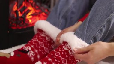 Kız şöminenin yanında otururken sıcak Noel çorapları giyer. Kış, yeni yıl konsepti. Şöminenin yanındaki Noel çoraplarının içinde ayaklar. Tatil kıyafetleri. Sıcak atmosferdeki kız. Kışlık ev kıyafetleri