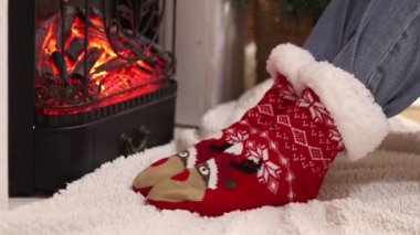 Sıcak Noel çoraplı kız şöminenin yanında oturuyor. Kış, yeni yıl konsepti. Şöminenin yanındaki Noel çoraplarının içinde ayaklar. Tatil kıyafetleri. Sıcak atmosferdeki kız. Kışlık ev kıyafetleri
