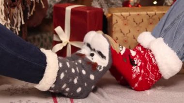 Kız arkadaşlar oynaşıyor, bacaklar birbirine yakın. Şenlikli çoraplı arkadaşlar Noel hediyelerinin yanındaki halıya otururlar. Noel atmosferi. Kış, yeni yıl konsepti. Şenlikli Yeni Yıl giysileri
