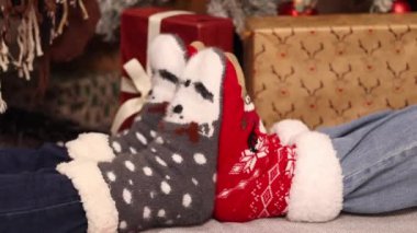 Kız arkadaşlar oynaşıyor, bacaklar birbirine yakın. Şenlikli çoraplı arkadaşlar Noel hediyelerinin yanındaki halıya otururlar. Noel atmosferi. Kış, yeni yıl konsepti. Şenlikli Yeni Yıl giysileri