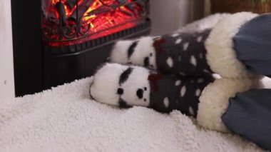 Sıcak Noel çoraplı kız şöminenin yanında oturuyor. Kış, yeni yıl konsepti. Şöminenin yanındaki Noel çoraplarının içinde ayaklar. Tatil kıyafetleri. Sıcak atmosferdeki kız. Kışlık ev kıyafetleri