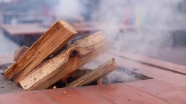 Panayırda özel bir masada odun yakmak. Ortasında odun yakmak için delik olan metal bir brazier, açık bir ateş. Yangına yakın çekim. Ateş yakıyorum, çok duman var.