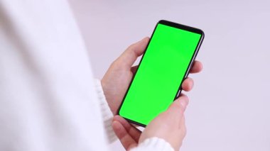 Yeşil ekranlı cep telefonu. Yeşil ekranlı akıllı telefonu tutan kadın eller, yakın plan. Beyaz arka planda telefonu olan beyaz kazaklı bir kız. Kromakey cep telefonunu tutan tanımlanamayan el