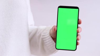 Yeşil ekranlı cep telefonu. Yeşil ekranlı akıllı telefonu tutan kadın eller, yakın plan. Beyaz arka planda telefonu olan beyaz kazaklı bir kız. Kromakey cep telefonunu tutan tanımlanamayan el