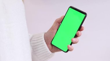 Yeşil ekranlı cep telefonu. Yeşil ekranlı akıllı telefonu tutan kadın eller, yakın plan. Beyaz arka planda telefonu olan beyaz kazaklı bir kız. Kromakey cep telefonunu tutan tanımlanamayan el