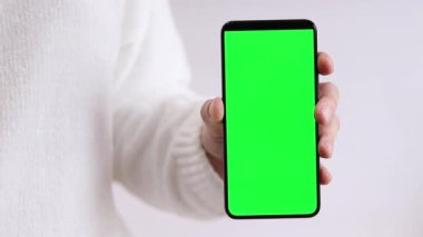 Yeşil ekranlı cep telefonu. Yeşil ekranlı akıllı telefonu tutan kadın eller, yakın plan. Beyaz arka planda telefonu olan beyaz kazaklı bir kız. Kromakey cep telefonunu tutan tanımlanamayan el