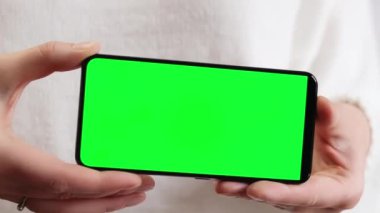 Yeşil ekranlı cep telefonu. Yeşil ekranlı akıllı telefonu tutan kadın eller, yakın plan. Beyaz arka planda telefonu olan beyaz kazaklı bir kız. Kromakey cep telefonunu tutan tanımlanamayan el